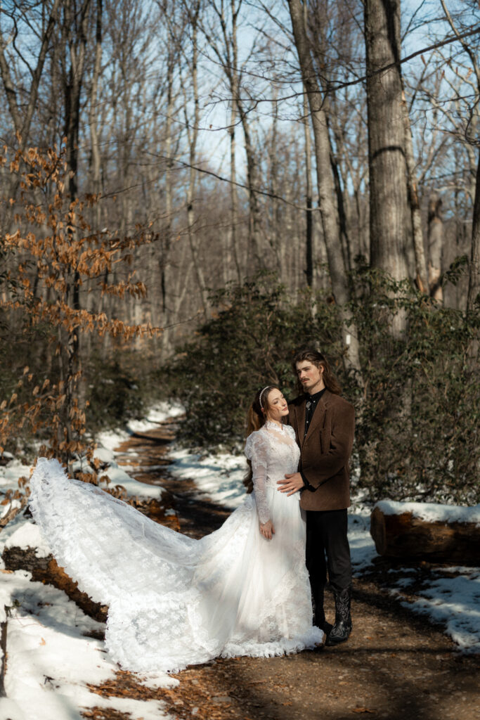 Cinematic photograph of an adventurous couple eloping in the forest, featuring the bride in a lace vintage wedding dress holding a floral bouquet while the groom is in a rustic suit. Captured by a destination wedding photographer in a documentary style.