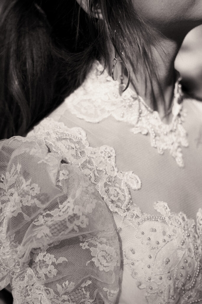 Cinematic photograph of an adventurous couple eloping in the forest, featuring the bride in a lace vintage wedding dress holding a floral bouquet while the groom is in a rustic suit. Captured by a destination wedding photographer in a documentary style.