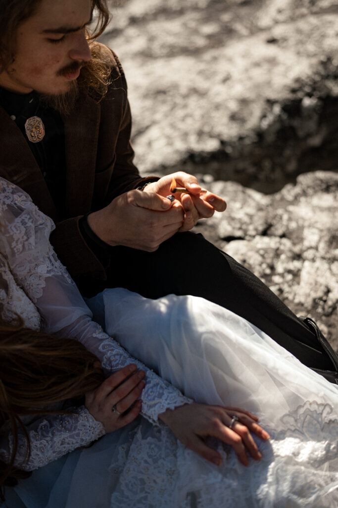 Cinematic photograph of an adventurous couple eloping in the forest, featuring the bride in a lace vintage wedding dress holding a floral bouquet while the groom is in a rustic suit. Captured by a destination wedding photographer in a documentary style.