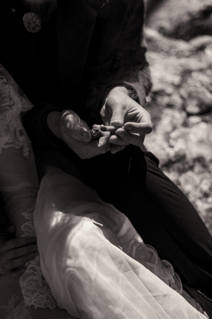 Cinematic photograph of an adventurous couple eloping in the forest, featuring the bride in a lace vintage wedding dress holding a floral bouquet while the groom is in a rustic suit. Captured by a destination wedding photographer in a documentary style.