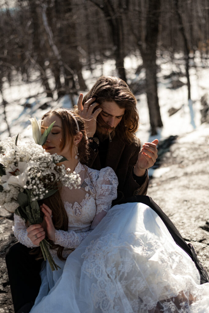 Cinematic photograph of an adventurous couple eloping in the forest, featuring the bride in a lace vintage wedding dress holding a floral bouquet while the groom is in a rustic suit. Captured by a destination wedding photographer in a documentary style.