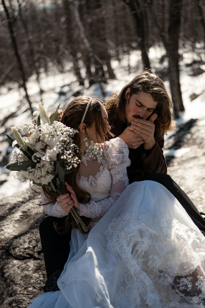 Cinematic photograph of an adventurous couple eloping in the forest, featuring the bride in a lace vintage wedding dress holding a floral bouquet while the groom is in a rustic suit. Captured by a destination wedding photographer in a documentary style.