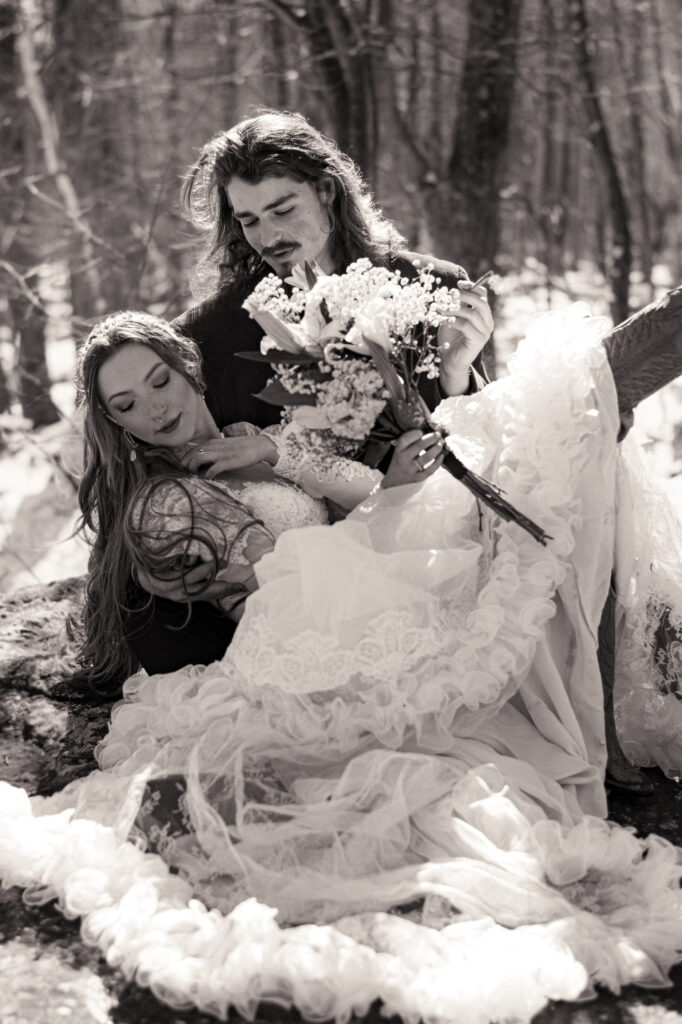 Cinematic photograph of an adventurous couple eloping in the forest, featuring the bride in a lace vintage wedding dress holding a floral bouquet while the groom is in a rustic suit. Captured by a destination wedding photographer in a documentary style.