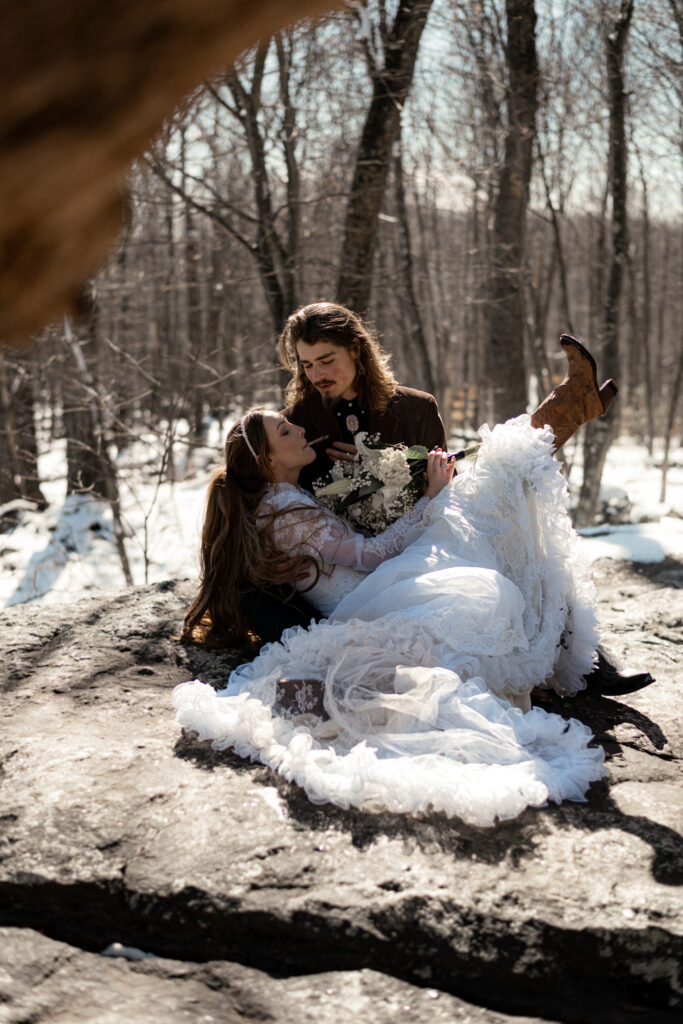 Cinematic photograph of an adventurous couple eloping in the forest, featuring the bride in a lace vintage wedding dress holding a floral bouquet while the groom is in a rustic suit. Captured by a destination wedding photographer in a documentary style.