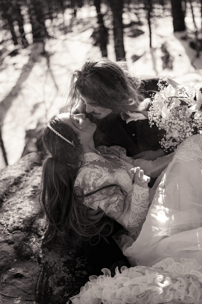 Cinematic photograph of an adventurous couple eloping in the forest, featuring the bride in a lace vintage wedding dress holding a floral bouquet while the groom is in a rustic suit. Captured by a destination wedding photographer in a documentary style.