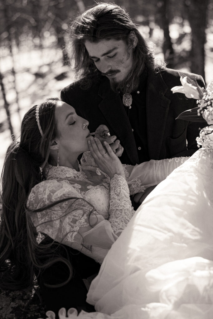 Cinematic photograph of an adventurous couple eloping in the forest, featuring the bride in a lace vintage wedding dress holding a floral bouquet while the groom is in a rustic suit. Captured by a destination wedding photographer in a documentary style.