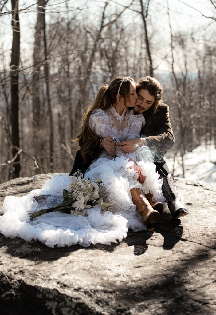 Cinematic photograph of an adventurous couple eloping in the forest, featuring the bride in a lace vintage wedding dress holding a floral bouquet while the groom is in a rustic suit. Captured by a destination wedding photographer in a documentary style.