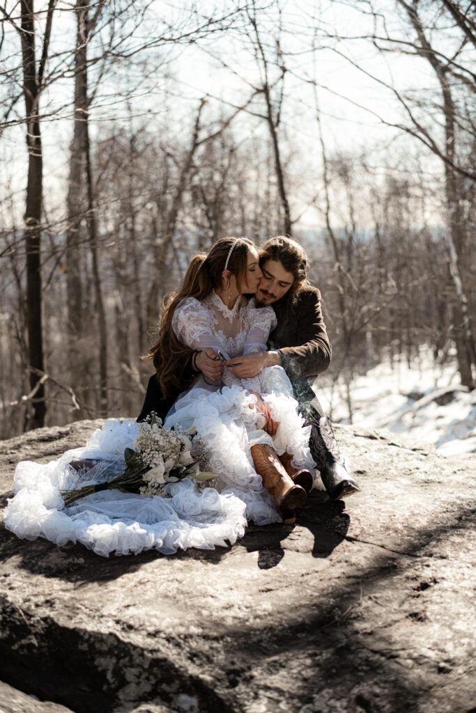 Cinematic photograph of an adventurous couple eloping in the forest, featuring the bride in a lace vintage wedding dress holding a floral bouquet while the groom is in a rustic suit. Captured by a destination wedding photographer in a documentary style.