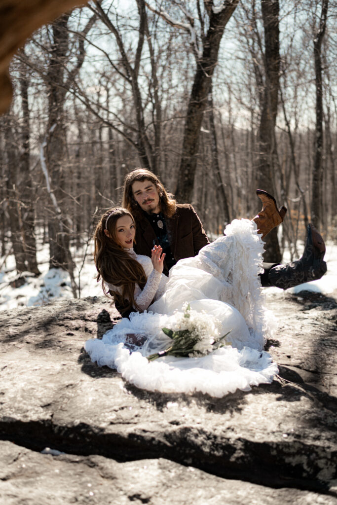 Cinematic photograph of an adventurous couple eloping in the forest, featuring the bride in a lace vintage wedding dress holding a floral bouquet while the groom is in a rustic suit. Captured by a destination wedding photographer in a documentary style.