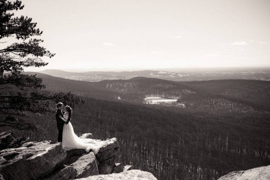 Cinematic photograph of an adventurous couple eloping in the forest, featuring the bride in a lace vintage wedding dress holding a floral bouquet while the groom is in a rustic suit. Captured by a destination wedding photographer in a documentary style.