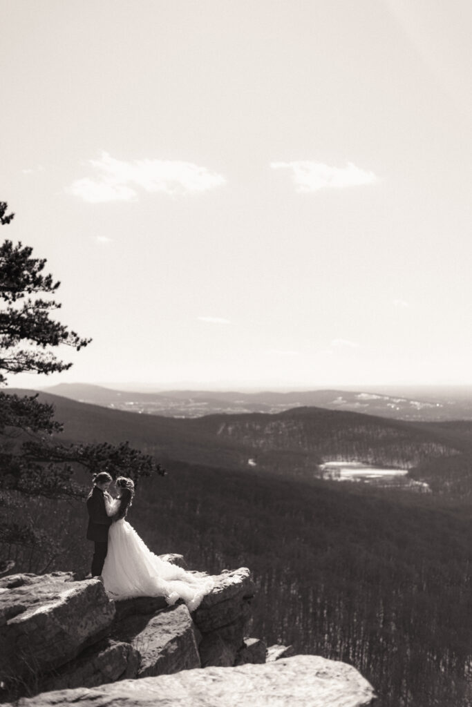 Cinematic photograph of an adventurous couple eloping in the forest, featuring the bride in a lace vintage wedding dress holding a floral bouquet while the groom is in a rustic suit. Captured by a destination wedding photographer in a documentary style.