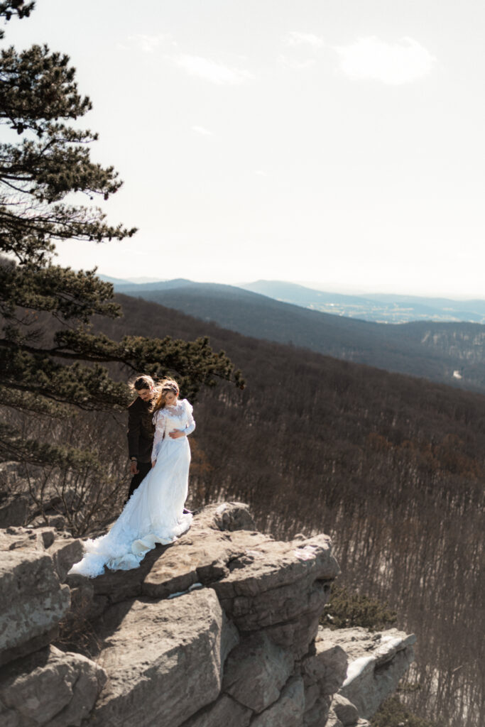 Cinematic photograph of an adventurous couple eloping in the forest, featuring the bride in a lace vintage wedding dress holding a floral bouquet while the groom is in a rustic suit. Captured by a destination wedding photographer in a documentary style.