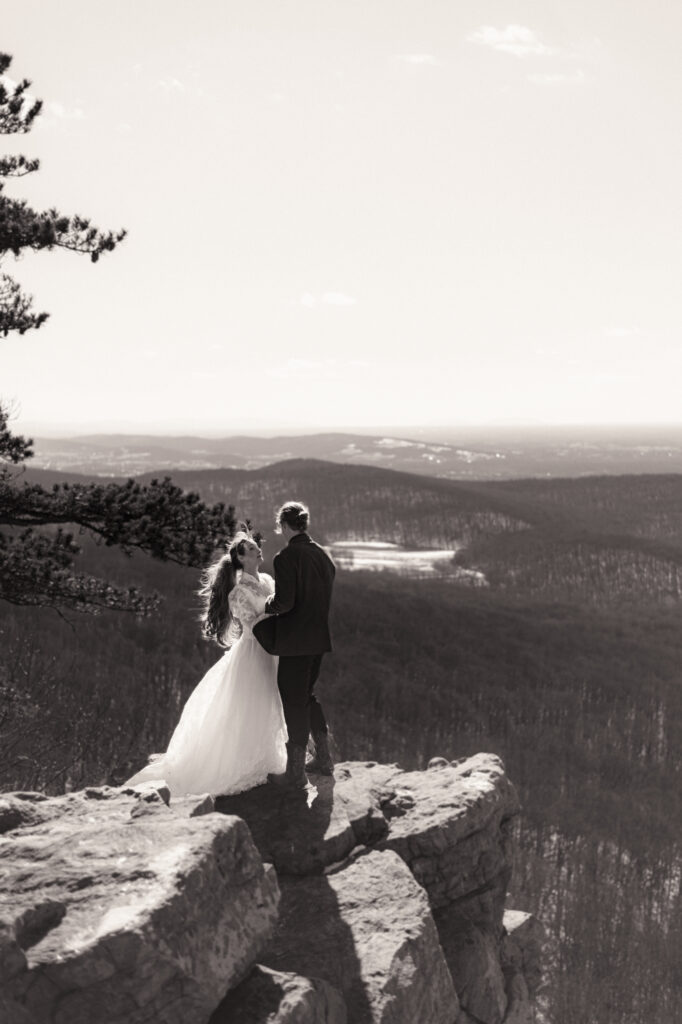 Cinematic photograph of an adventurous couple eloping in the forest, featuring the bride in a lace vintage wedding dress holding a floral bouquet while the groom is in a rustic suit. Captured by a destination wedding photographer in a documentary style.