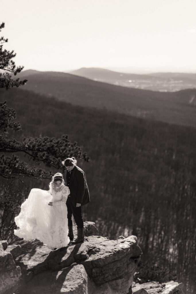 Cinematic photograph of an adventurous couple eloping in the forest, featuring the bride in a lace vintage wedding dress holding a floral bouquet while the groom is in a rustic suit. Captured by a destination wedding photographer in a documentary style.