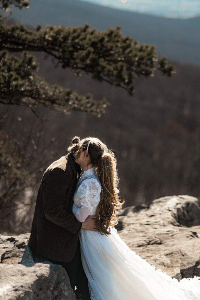 Cinematic photograph of an adventurous couple eloping in the forest, featuring the bride in a lace vintage wedding dress holding a floral bouquet while the groom is in a rustic suit. Captured by a destination wedding photographer in a documentary style.