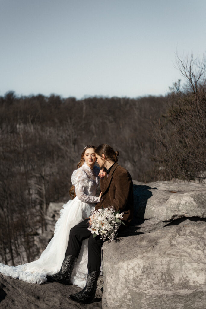 Cinematic photograph of an adventurous couple eloping in the forest, featuring the bride in a lace vintage wedding dress holding a floral bouquet while the groom is in a rustic suit. Captured by a destination wedding photographer in a documentary style.