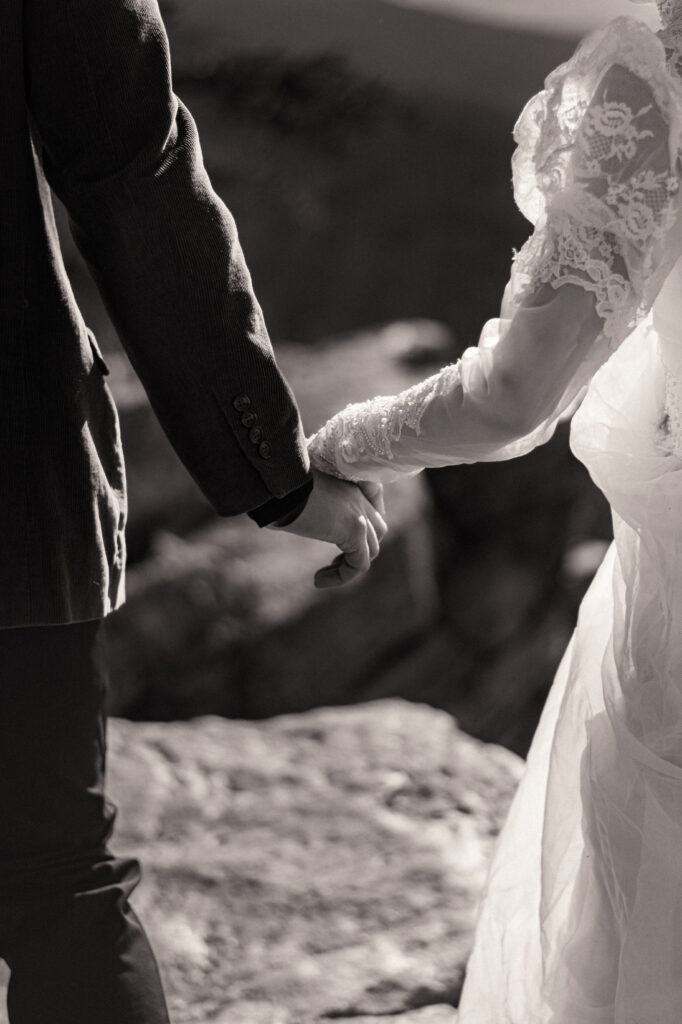 Cinematic photograph of an adventurous couple eloping in the forest, featuring the bride in a lace vintage wedding dress holding a floral bouquet while the groom is in a rustic suit. Captured by a destination wedding photographer in a documentary style.