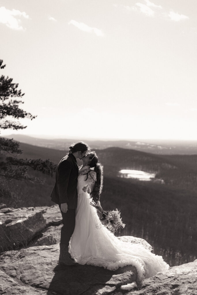 Cinematic photograph of an adventurous couple eloping in the forest, featuring the bride in a lace vintage wedding dress holding a floral bouquet while the groom is in a rustic suit. Captured by a destination wedding photographer in a documentary style.