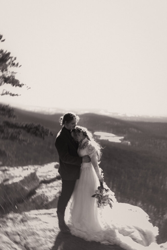 Cinematic photograph of an adventurous couple eloping in the forest, featuring the bride in a lace vintage wedding dress holding a floral bouquet while the groom is in a rustic suit. Captured by a destination wedding photographer in a documentary style.