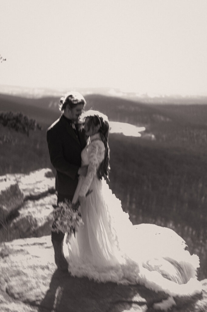 Cinematic photograph of an adventurous couple eloping in the forest, featuring the bride in a lace vintage wedding dress holding a floral bouquet while the groom is in a rustic suit. Captured by a destination wedding photographer in a documentary style.