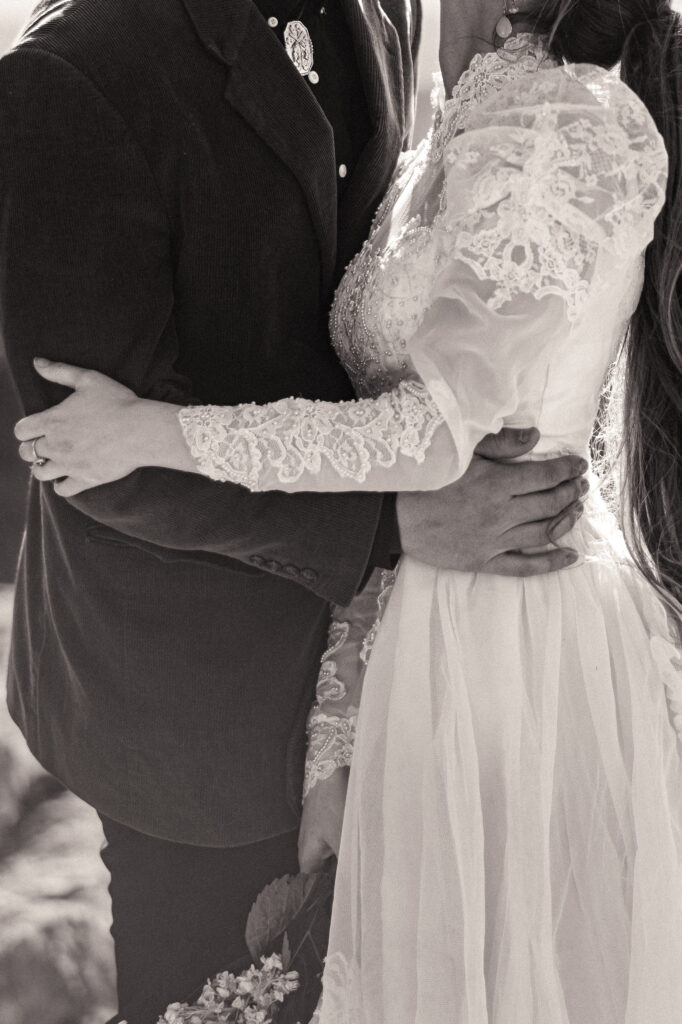 Cinematic photograph of an adventurous couple eloping in the forest, featuring the bride in a lace vintage wedding dress holding a floral bouquet while the groom is in a rustic suit. Captured by a destination wedding photographer in a documentary style.