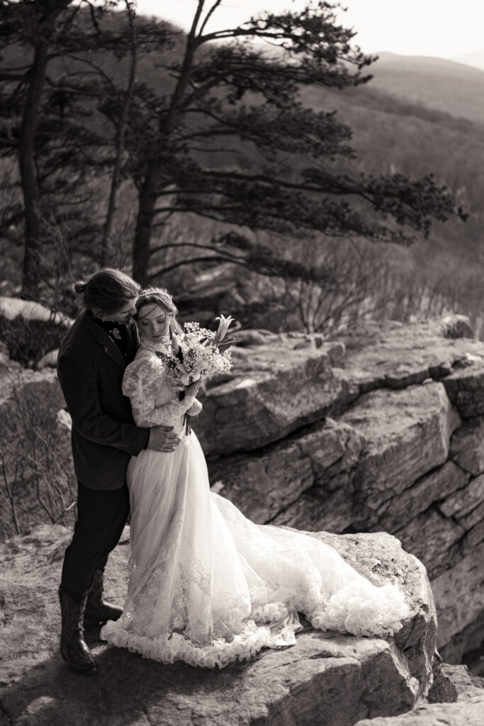 Cinematic photograph of an adventurous couple eloping in the forest, featuring the bride in a lace vintage wedding dress holding a floral bouquet while the groom is in a rustic suit. Captured by a destination wedding photographer in a documentary style.