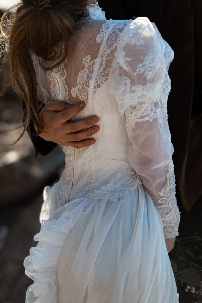 Cinematic photograph of an adventurous couple eloping in the forest, featuring the bride in a lace vintage wedding dress holding a floral bouquet while the groom is in a rustic suit. Captured by a destination wedding photographer in a documentary style.