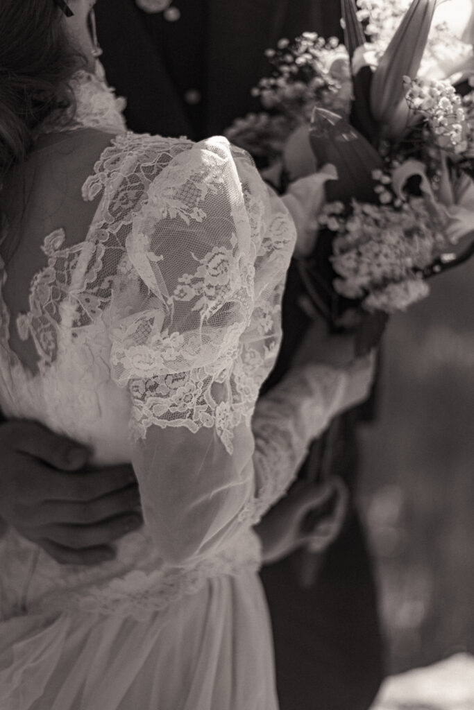 Cinematic photograph of an adventurous couple eloping in the forest, featuring the bride in a lace vintage wedding dress holding a floral bouquet while the groom is in a rustic suit. Captured by a destination wedding photographer in a documentary style.