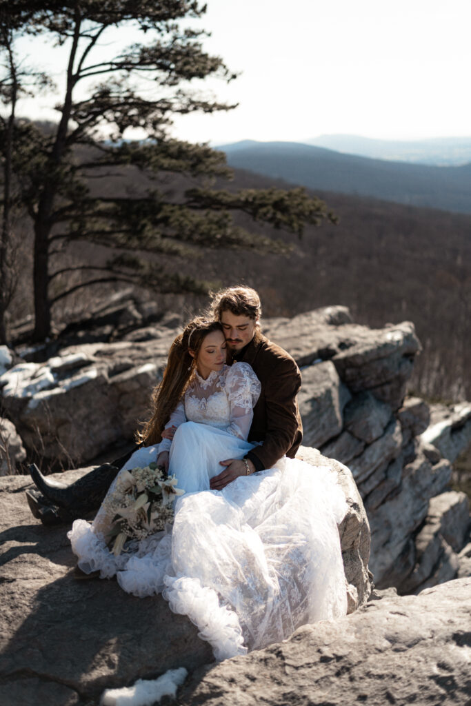 Cinematic photograph of an adventurous couple eloping in the forest, featuring the bride in a lace vintage wedding dress holding a floral bouquet while the groom is in a rustic suit. Captured by a destination wedding photographer in a documentary style.