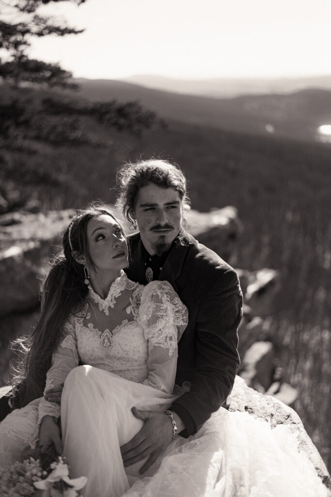 Cinematic photograph of an adventurous couple eloping in the forest, featuring the bride in a lace vintage wedding dress holding a floral bouquet while the groom is in a rustic suit. Captured by a destination wedding photographer in a documentary style.