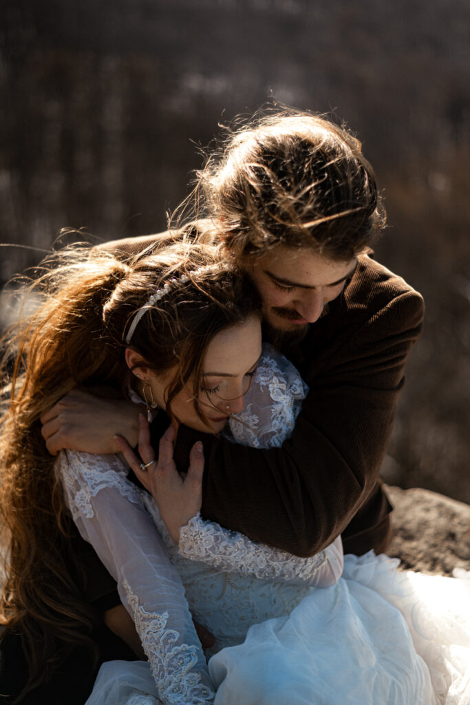 Cinematic photograph of an adventurous couple eloping in the forest, featuring the bride in a lace vintage wedding dress holding a floral bouquet while the groom is in a rustic suit. Captured by a destination wedding photographer in a documentary style.