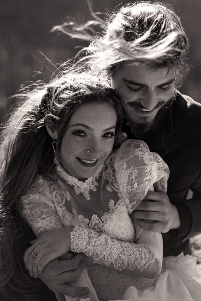 Cinematic photograph of an adventurous couple eloping in the forest, featuring the bride in a lace vintage wedding dress holding a floral bouquet while the groom is in a rustic suit. Captured by a destination wedding photographer in a documentary style.