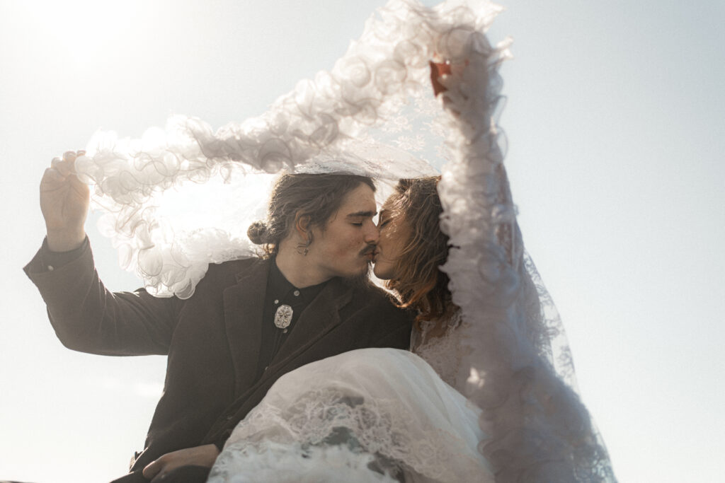 Cinematic photograph of an adventurous couple eloping in the forest, featuring the bride in a lace vintage wedding dress holding a floral bouquet while the groom is in a rustic suit. Captured by a destination wedding photographer in a documentary style.